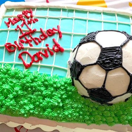 Photo of a soccer field shaped birthday cake with an edible soccer ball on the top
